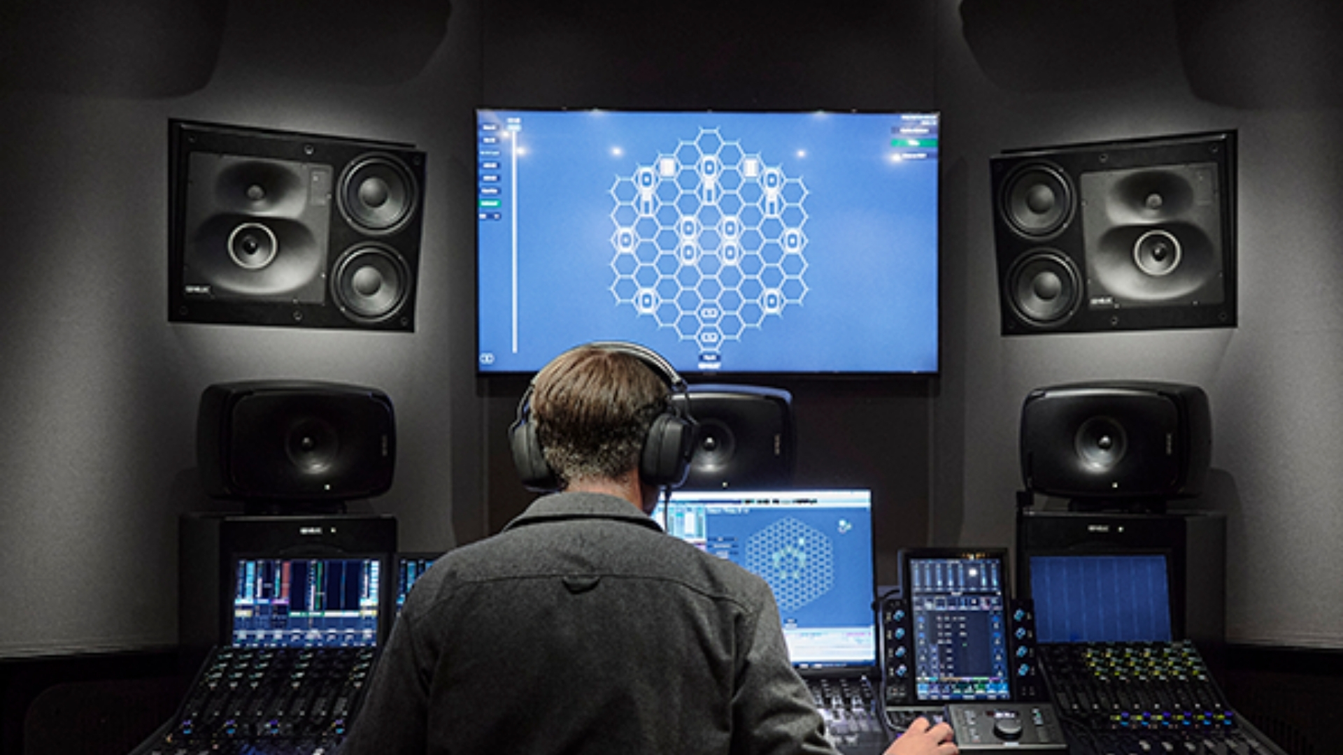 Engineer in a professional control room with multiple Genelec studio monitors and on-screen calibration software
