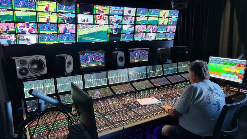 Broadcast audio engineer operating Calrec mixing console in live sports production facility